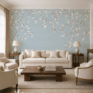 The Whispering Branches wallpaper mural in Dusty Blue covering a feature wall in a living room behind a cream sofa and armchairs. view-livingroom