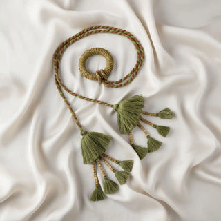 Flat lay of the Woodland Essence Tieback showing the jute-wrapped central ring and the braided green and brown cord on a satin background.