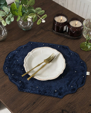 Close-up of a Zarfshan navy velvet placemat under a scalloped plate with crossed gold cutlery.