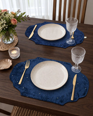 Two Zarfshan navy velvet placemats set with cream plates, crystal glasses and a tealight candle.