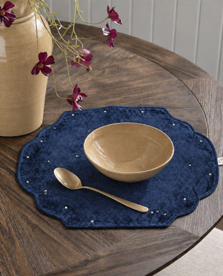 A single Zarfshan navy velvet placemat on a round wooden table, styled with a tan bowl and brass spoon.