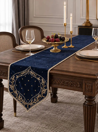 The Zarfshan Velvet Table Runner in Navy & Gold on a carved dining table with brass candlesticks and a bowl of cherries.