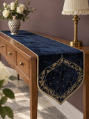 The Zarfshan Velvet Table Runner in Navy & Gold on a wooden console table with a silver vase of roses and a brass lamp.