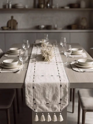 The Zarin Trace runner and placemat set in Natural & Black arranged on a dining table with ceramic dinnerware, glassware and a floral centrepiece, viewed from above.