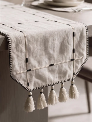 A detailed macro close-up of the Zarin Trace table runner highlighting the couched cord border, black whipstitch edge and beaded tassel fringe.