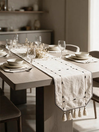 The Zarin Trace table runner in Natural & Black styled along a wooden dining table set with ceramic dinnerware, wine glasses and a dried floral centrepiece.