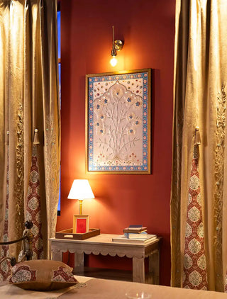 The Zarquash curtain in gold with silver leaf vines, pearl-like beads and a red floral medallion border, hung beside a red wall and bedside table.