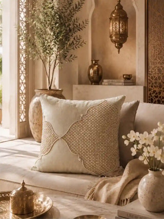 The Zayan Weave cushion cover in Ivory & Natural on a cream sofa beside a potted olive tree, a brass lantern and a vase of white flowers.