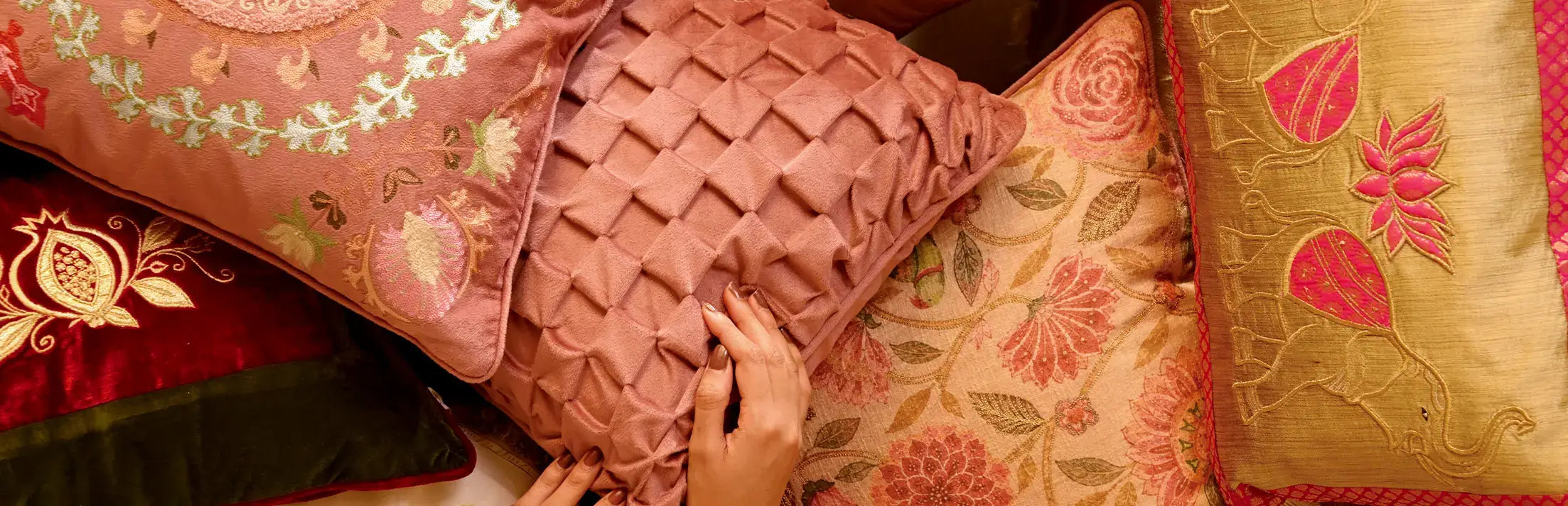 Hand resting on a pleated rose cushion among embroidered and floral silk cushions