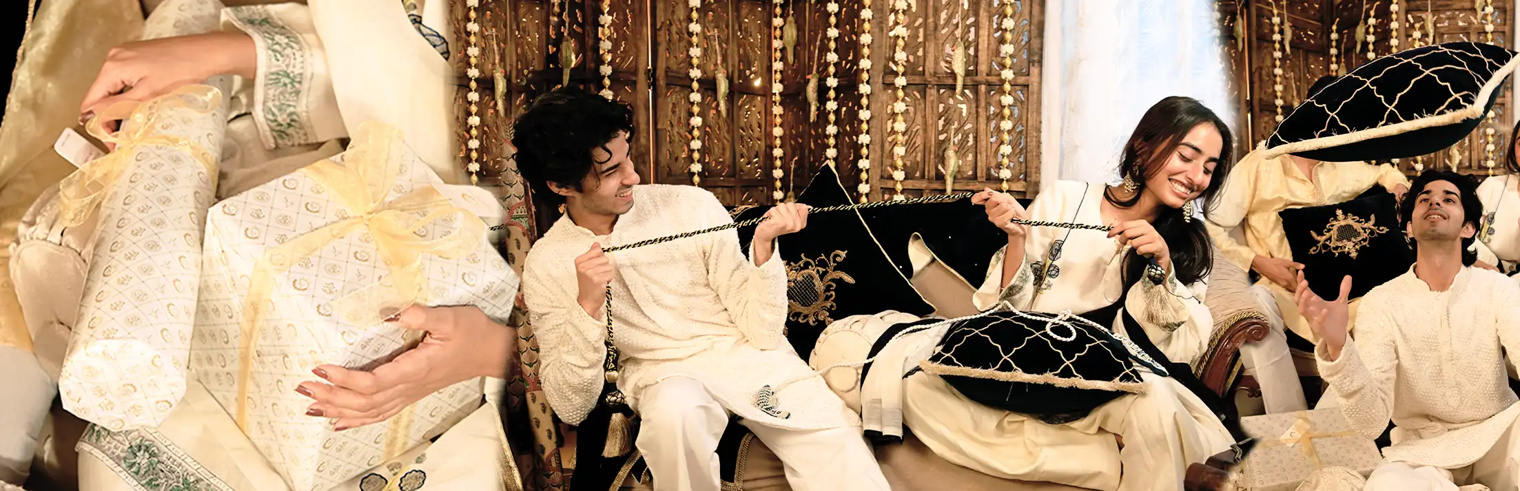 Hands holding gift boxes wrapped in ivory and gold, beside people in ivory festive clothes playing with black velvet cushions on a sofa